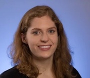 Anya Swanson, white woman shown from shoulders up smiling, shoulder length brown hair, blue background