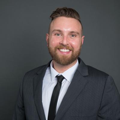 Robert Carroll headshot, man facing forward with beard, smiling, wearing a suit, shown from the shoulders up