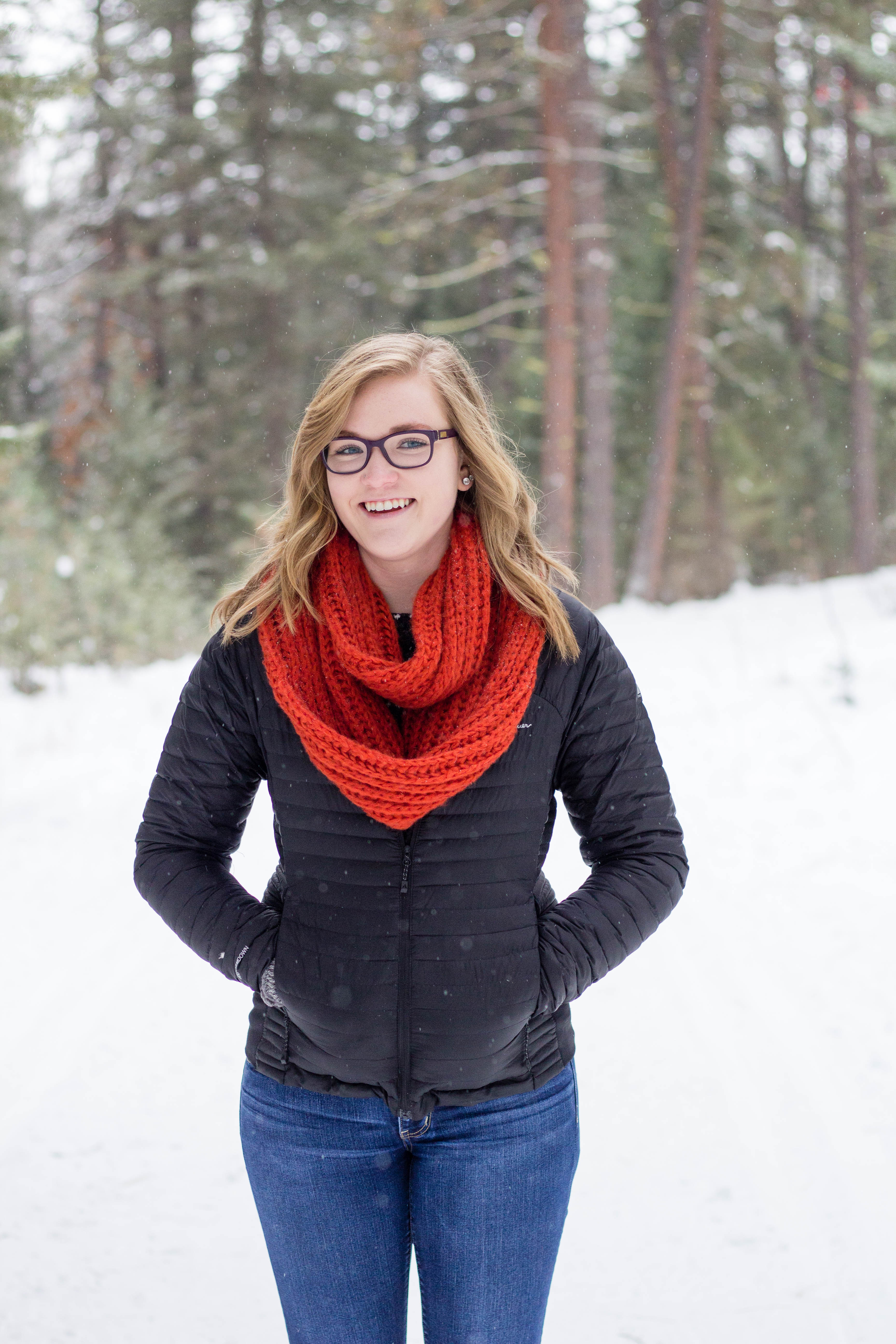 Headshot of Nicole Kirschten, a white woman with long, blonde hair wearing glasses, a red scarf, black coat, and jeans smiling at the camera.