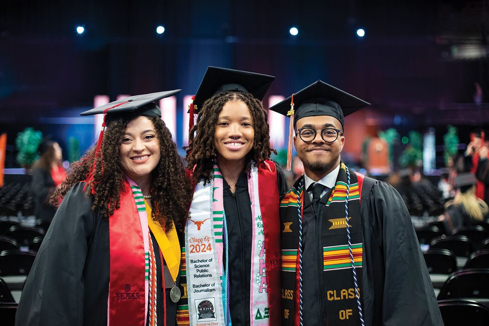 three Moody College graduates standing together in a row in their caps and gowns