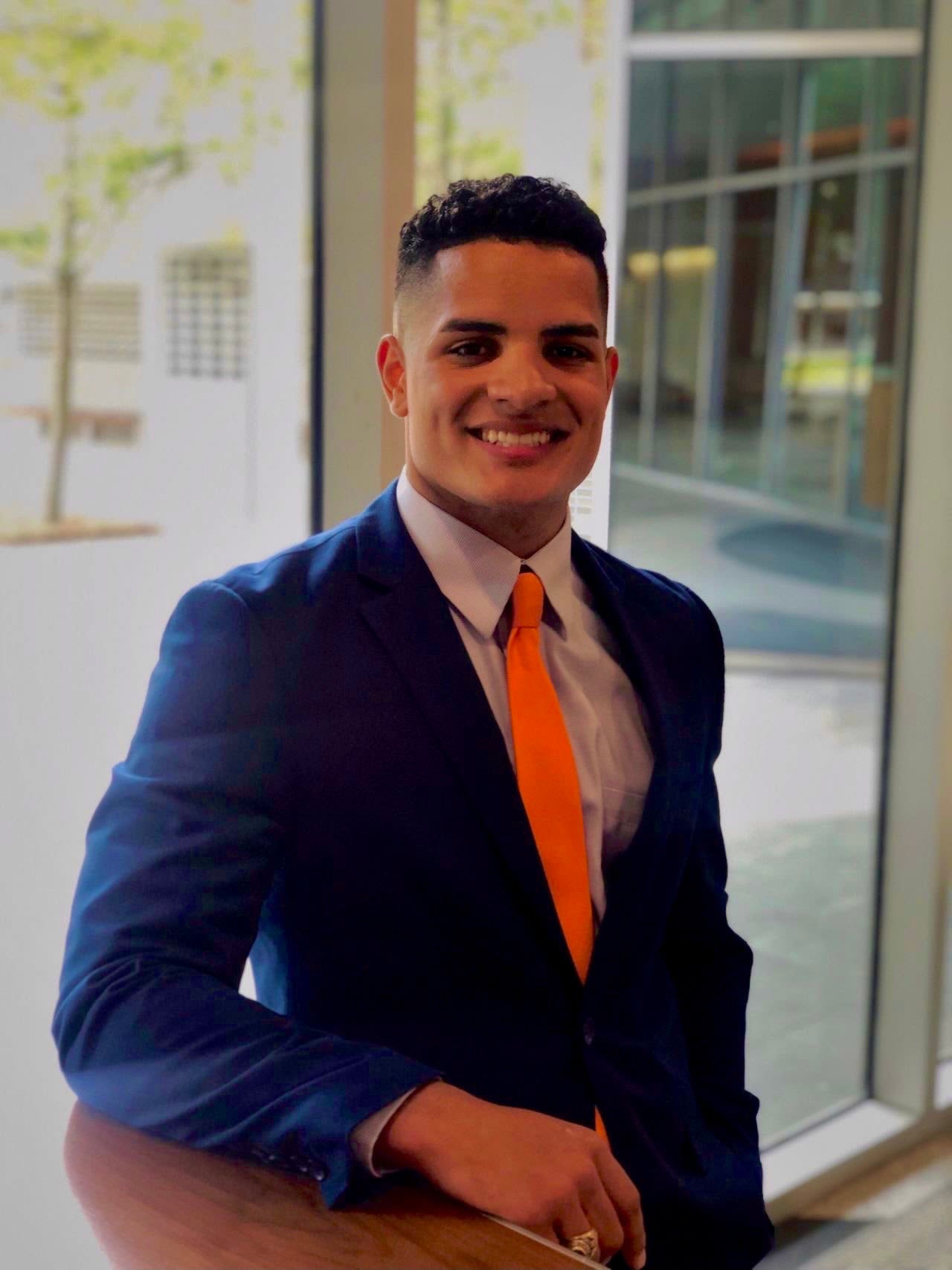 alumni taking a portrait in a suit with orange tie