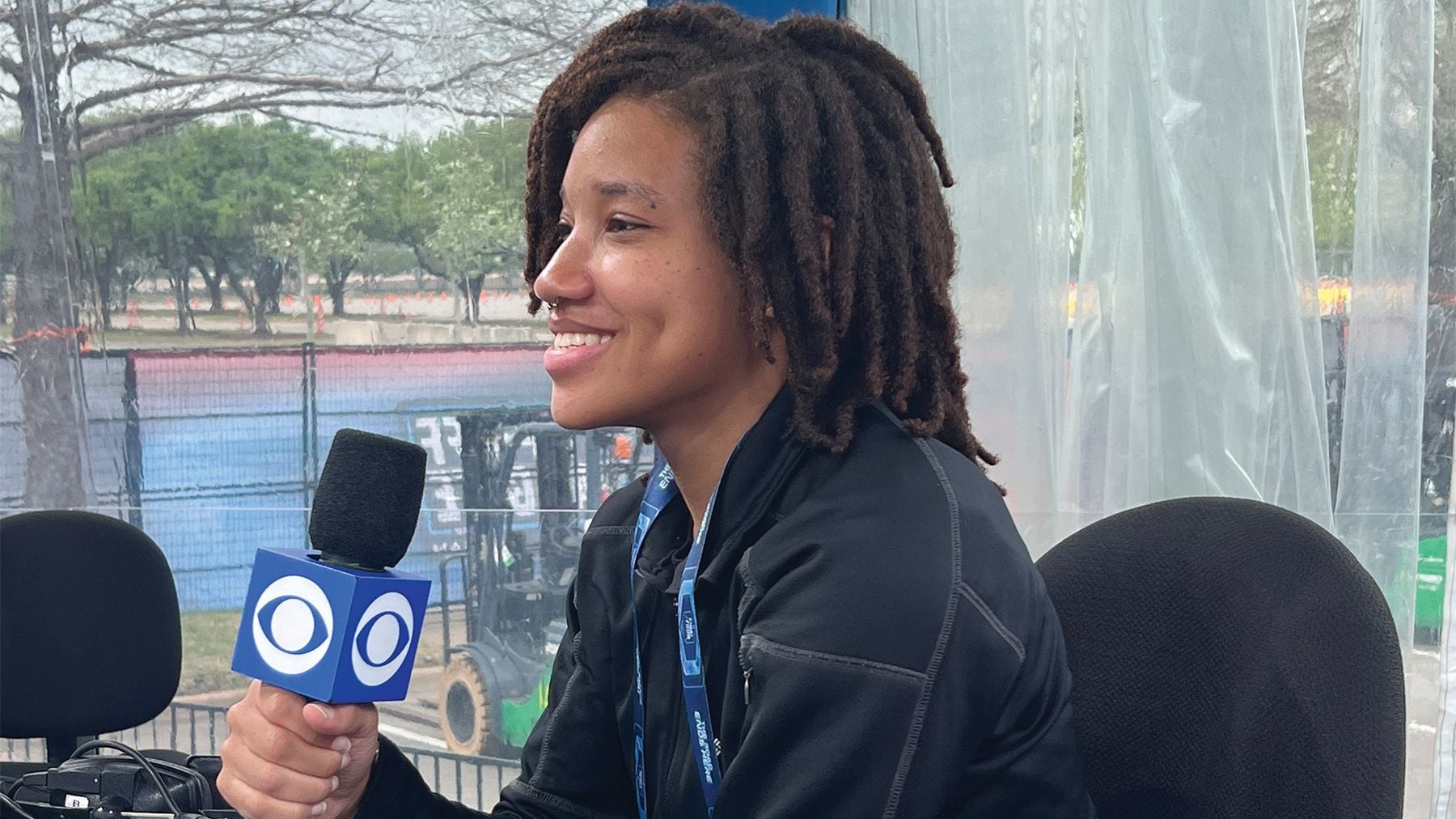 Student Madison Morris smiles in front of a camera holding a mic at her internship