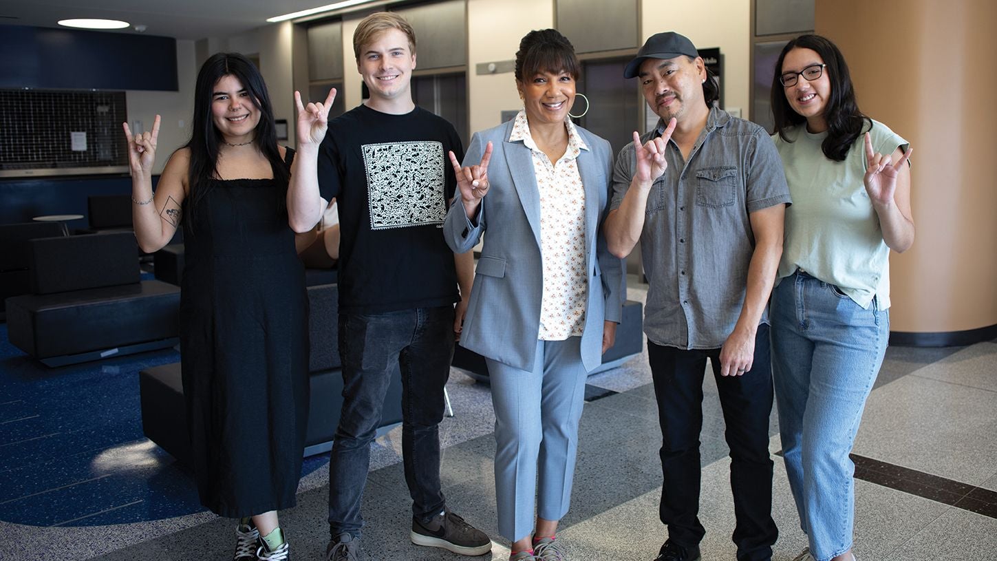 Moody College visitors Arthel Neville and Taku poses with students with hook em sign
