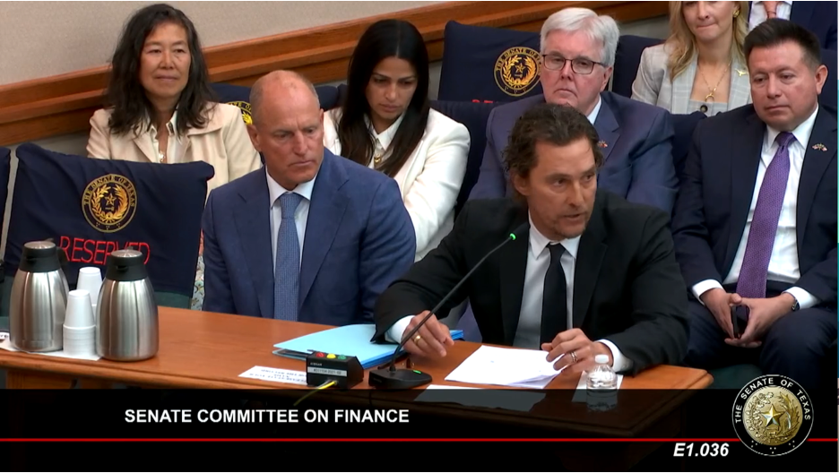Actors Matthew McConaughey and Woody Harrelson sit at desk in suits with microphones to address the Texas legislature.