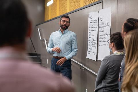 Attendees of the 2022 Health Communication Leadership Institute standing in front of two large pieces of paper on the wall with writing on them presenting their group idea regarding a case study.