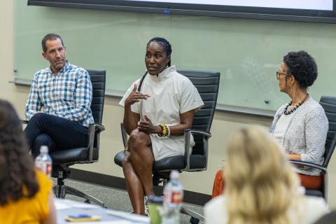 Two Black women and a white man sitting in office chairs at the front of a lecture hall speaking to the attendees at the Health Communication Leadership Institute.