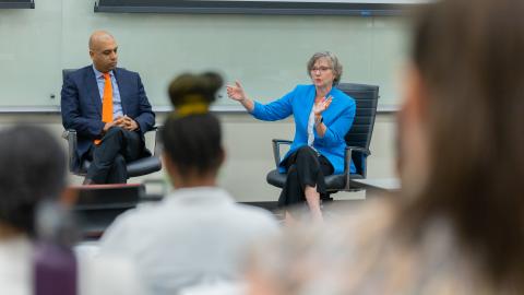A man and a woman sitting in chairs at the front of a room speaking to a crowd at the Health Communication Leadership Institute.