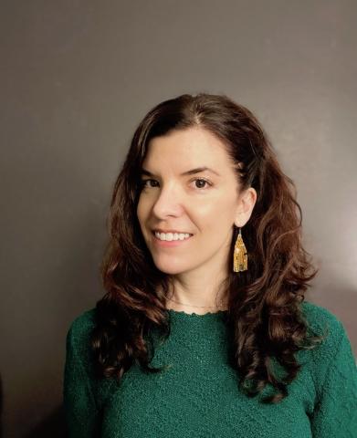 Headshot of Lauren Pezzullo, a white woman with long, curly, brown hair wearing a green sweater and gold earrings smiling at the camera.