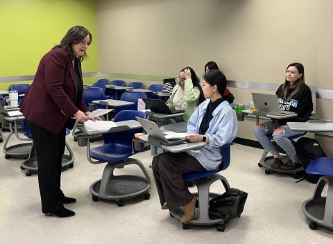 Dr. Stephens standing on the left side of the photo speaking with seated students on the right side of the photo