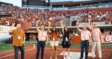 outstanding young texas exes standing on the football field with horns up 