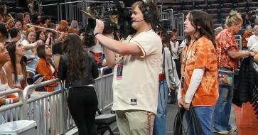 BVP student standing with a camera at a basketball at the moody center