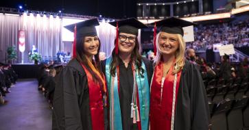 three moody graduates standing inside the moody center on graduation day