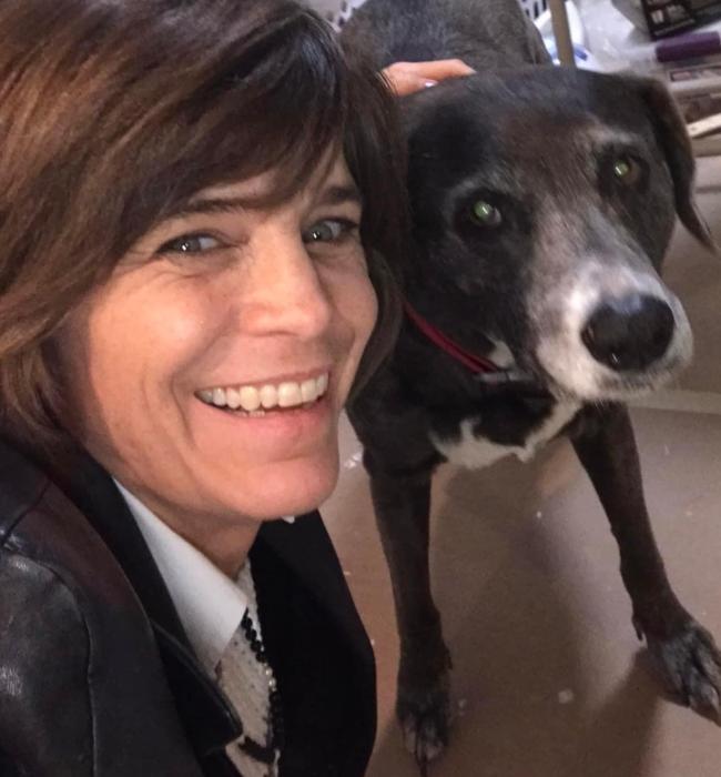 A woman, Karen Schlag, smiling for the camera next to with brown hair next to a black dog with white around it's mouth