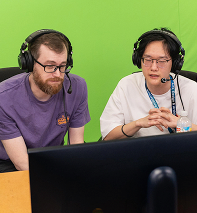 Two people sit at a computer with headsets on playing esports.