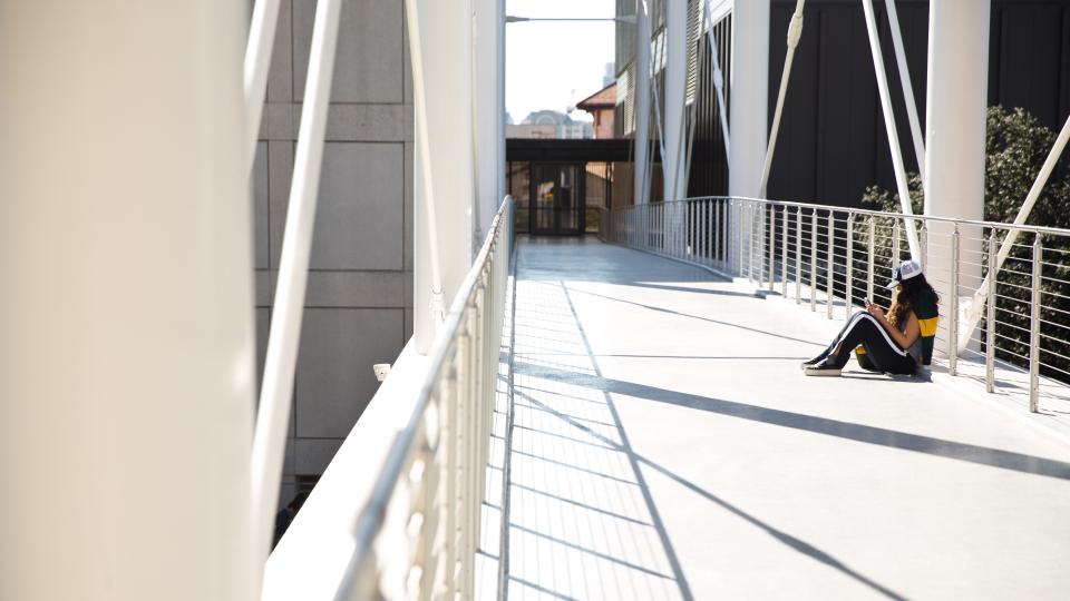 A student sits on the pedestrian bridge at Moody College of Communication.