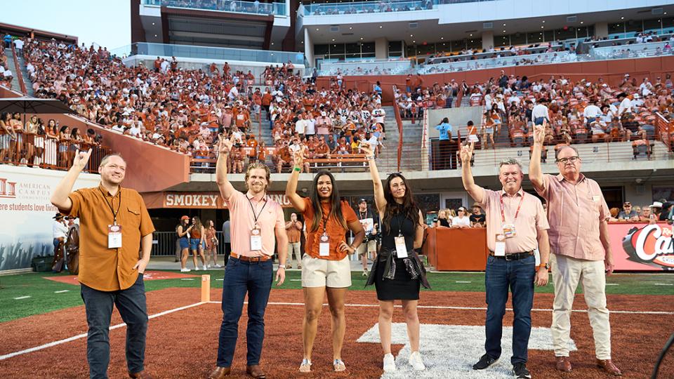 outstanding young texas exes standing on the football field with horns up 