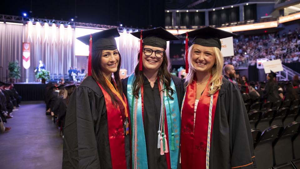 three moody graduates standing inside the moody center on graduation day