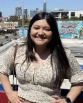A young woman with long brown hair standing before a skyline