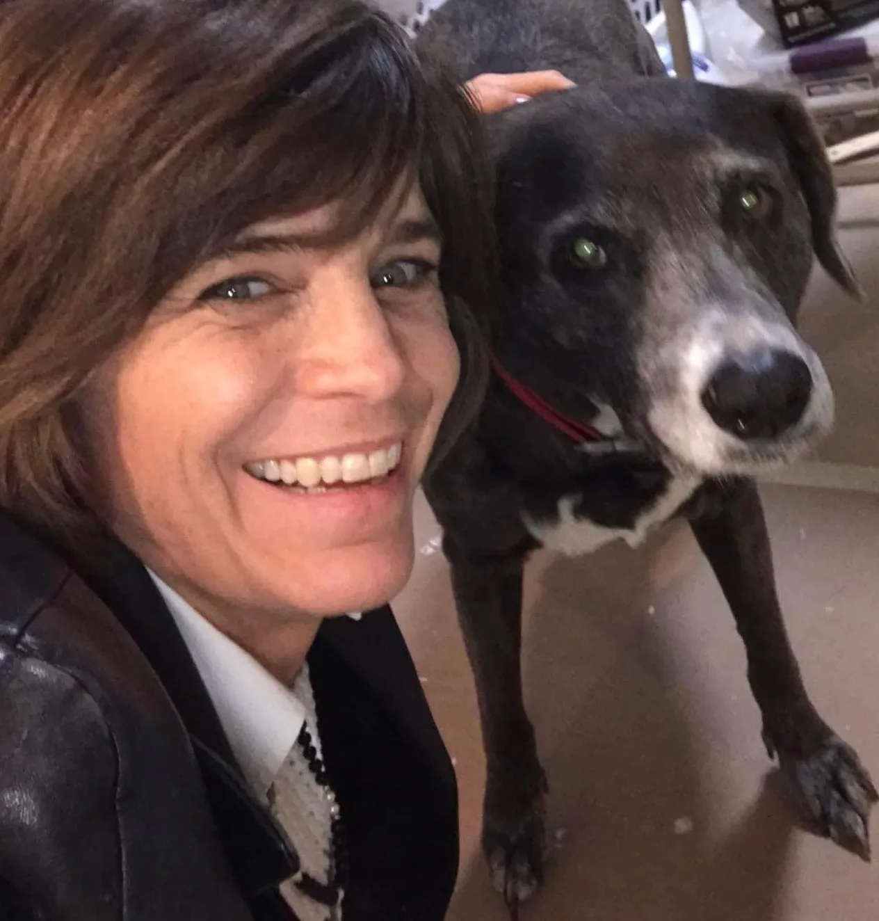 A woman, Karen Schlag, smiling for the camera next to with brown hair next to a black dog with white around it's mouth