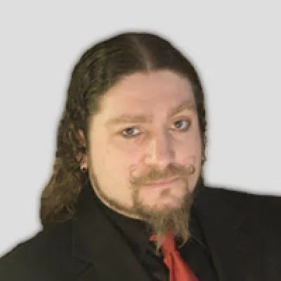 Josh Gunn headshot, man with shoulder length brown hair, facial hair, black shirt and red tie, looking at the camera