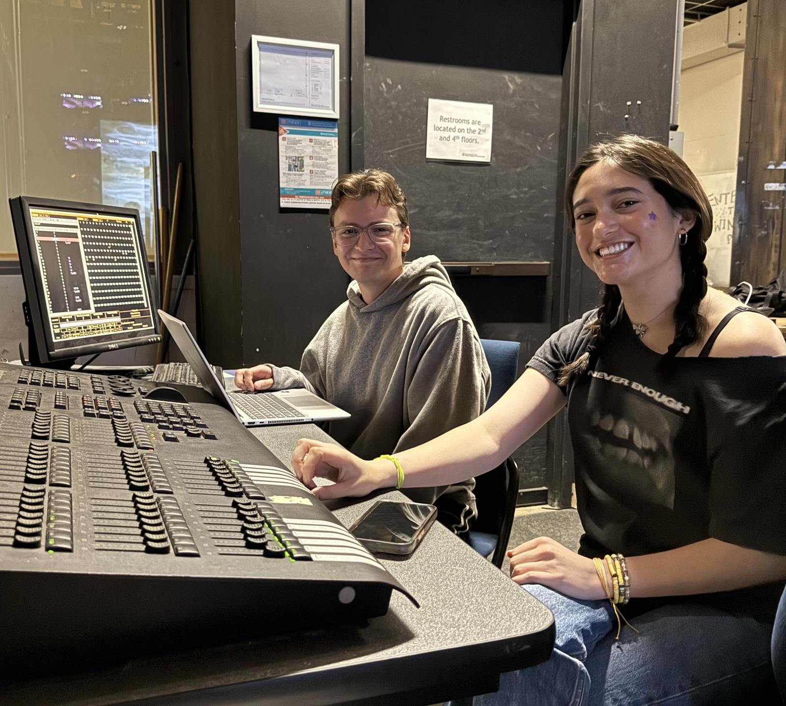 Two students sit behind a machine and smile for the camera while preparing for the Red River Reverb show