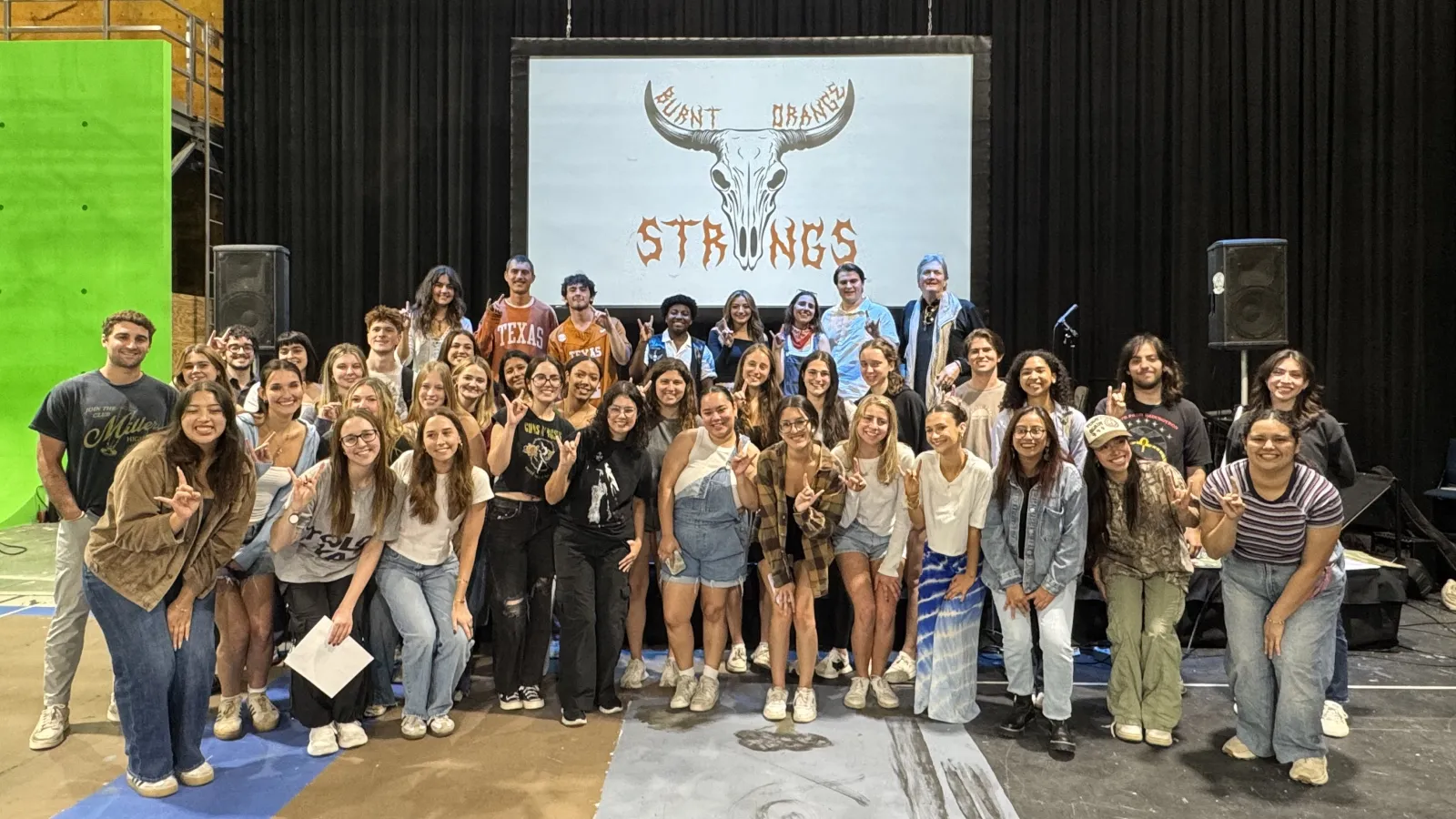 The full class of students smiling for a group photo in front of the Moody Groove stage set