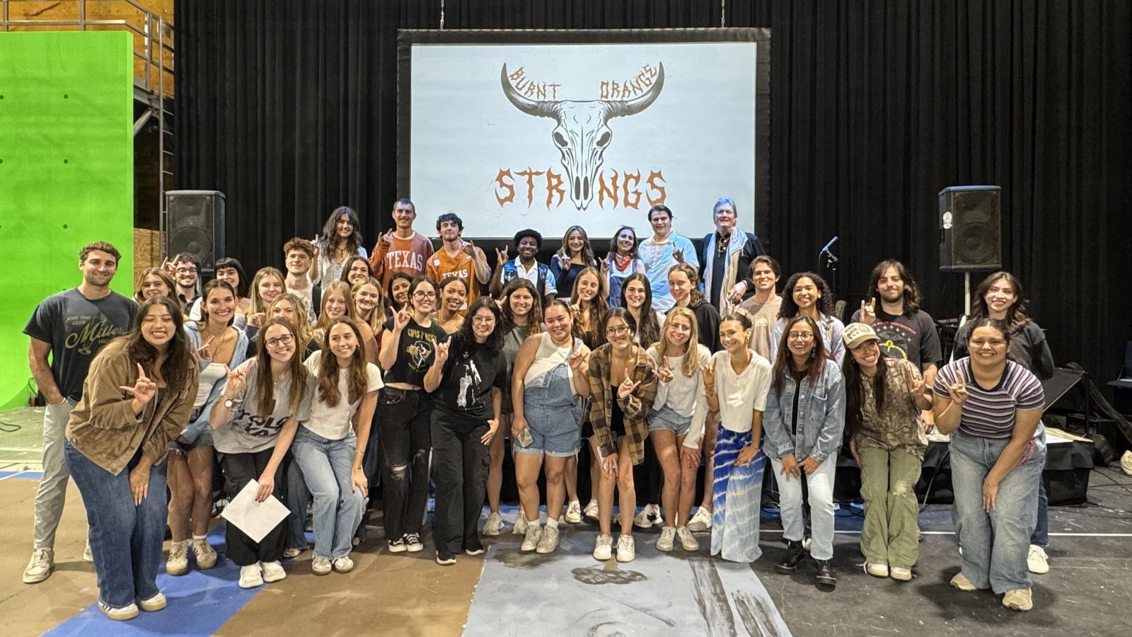 The full class of students smiling for a group photo in front of the Moody Groove stage set