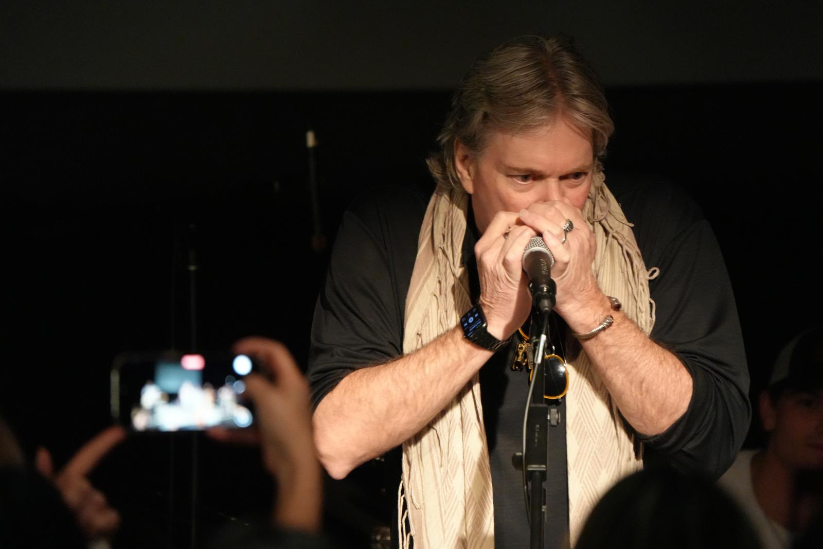 Image depicts man playing harmonica.