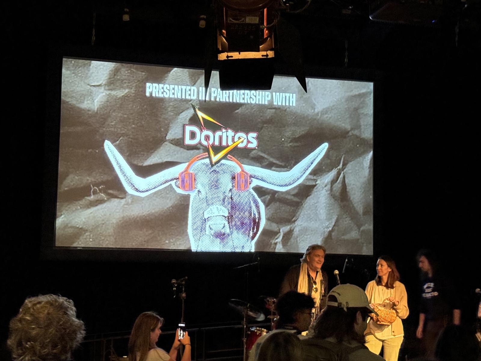 Image depicts two people on a stage with a concert logo behind to indicate the sponsor of the concert.