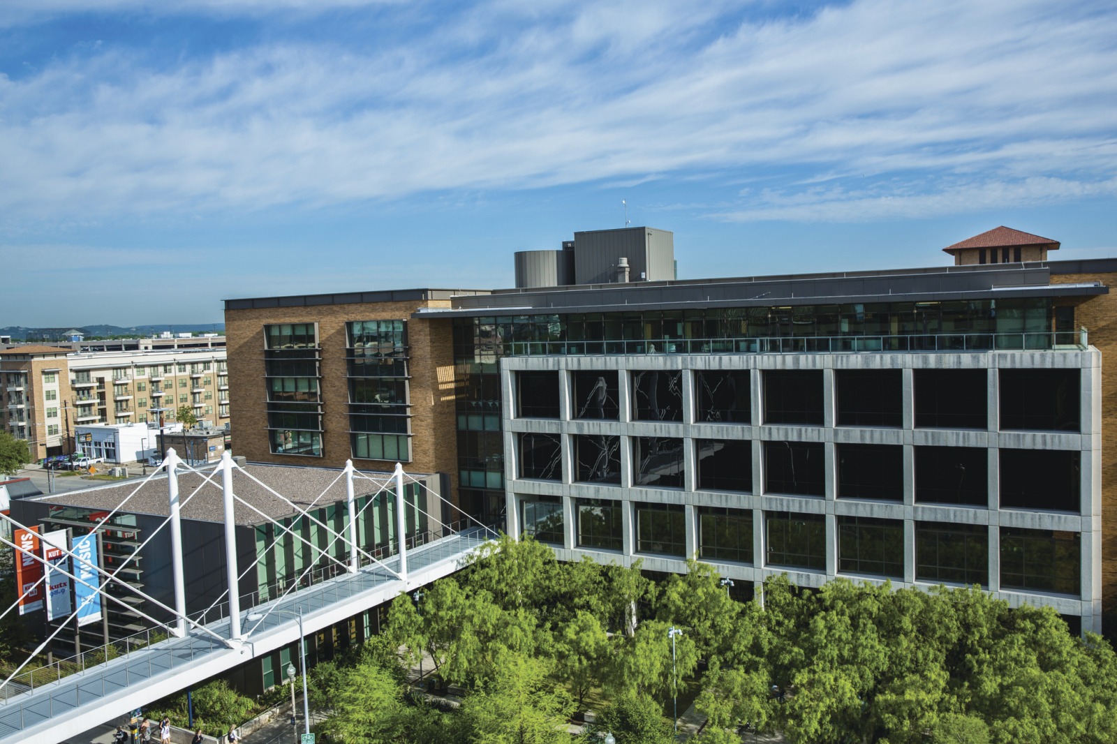 Moody College buildings and the pedestrian bridge above a tree-filled courtyard.