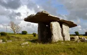 Stone sculpture on grassy hillside under a cloudy sky.