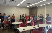 Image depicts students grouped in corners of the classroom discussing a topic.