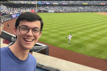 Scott Fonseka, Blue Shirt, standing in front of a baseball field