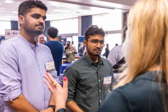 Two students stand listening to a recruiter