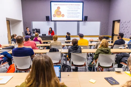 Conference room with seated attendees, powerpoint and two presenters (Lesley Willard and Wenhong Chen) at the front of the room