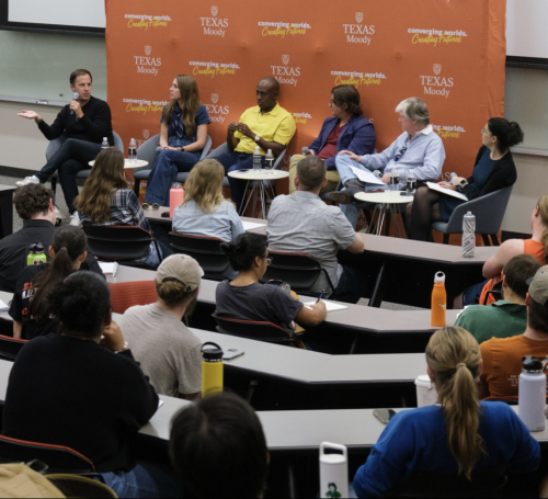 Six Panelists talking to one another at the front of a classroom, orange banner behind them