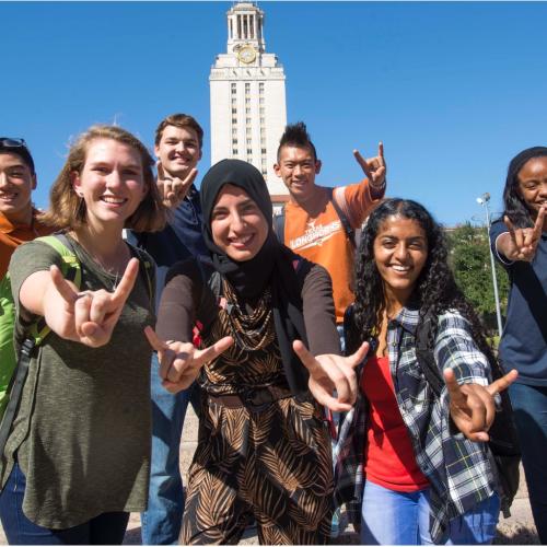 Group of students giving the hook 'em symbol in front of the UT tower