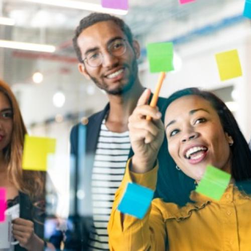 five people smiling and looking at a window with sticky notes 