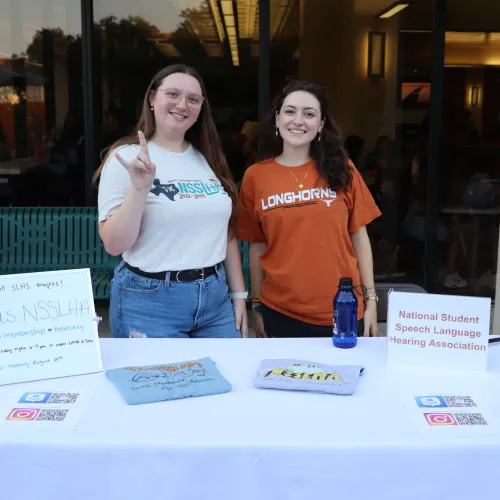 twostudentsbehindtablewithhookemsign