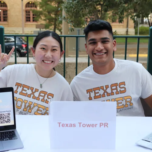 studentsbehindtabledoinghookemsign