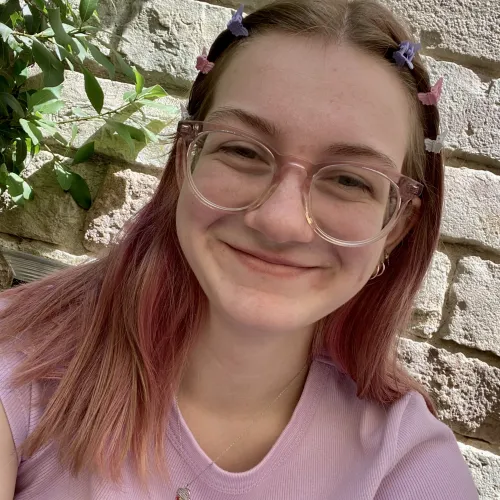 A young women with glasses and blonde hair with pink tips