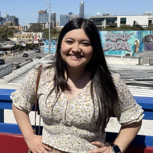 A young woman with long brown hair standing before a skyline