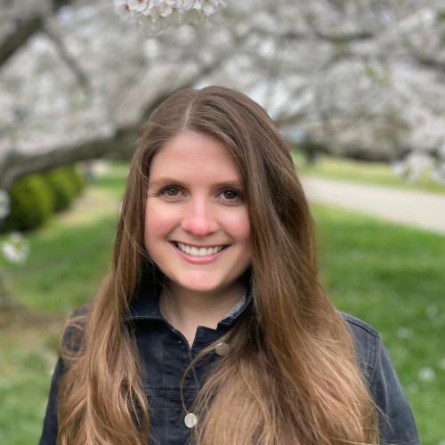 Woman smiling for her headshot in front of a floral tree with white flowers