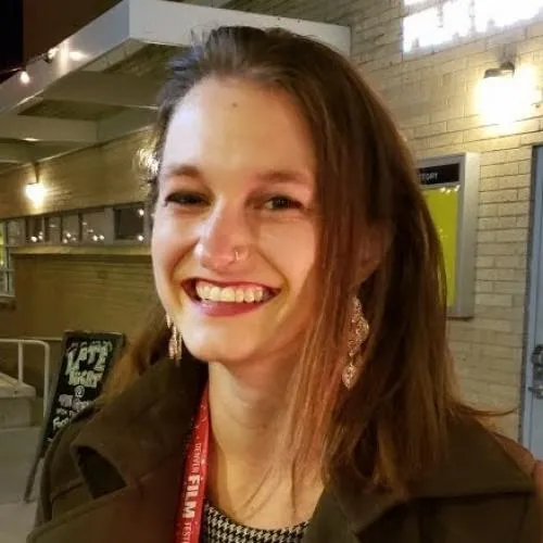 Hannah Wold Profile Picture, Brown hair, green coat, in front of a tan brick wall