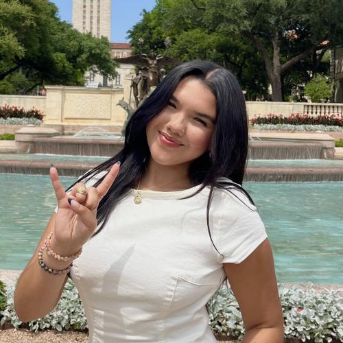 Young woman doing the Hook 'em Horns sign in front of the UT Tower and fountain