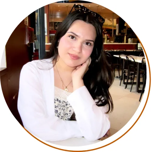 Andrea Alarcon Headshot, Wasit up, white cardigan and black and white shirt, long dark hair, sitting in a restaurant