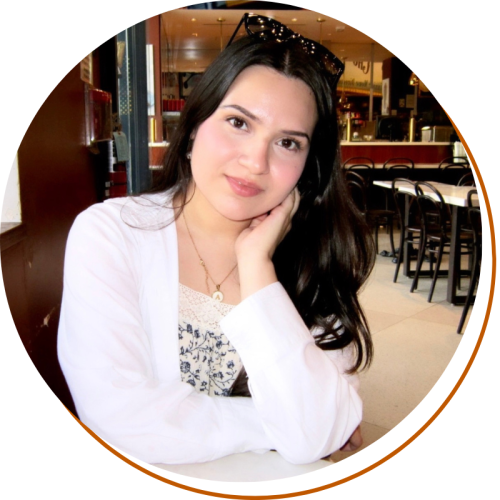 Andrea Alarcon Headshot Andrea Alarcon Headshot, Wasit up, white cardigan and black and white shirt, long dark hair, sitting in a restaurant