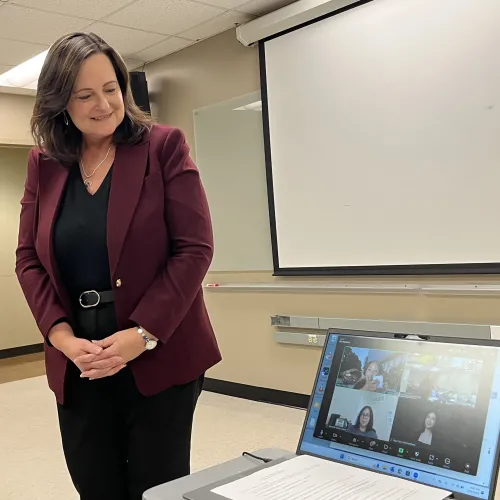 Dr. Stephens smiling at a laptop with hybrid students video calls 