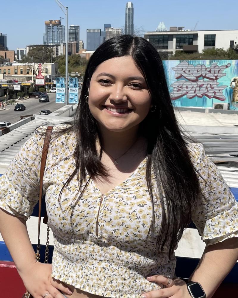 A young woman with long brown hair standing before a skyline