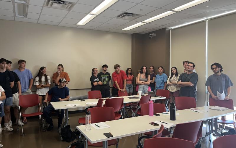 Image depicts students grouped in corners of the classroom discussing a topic.